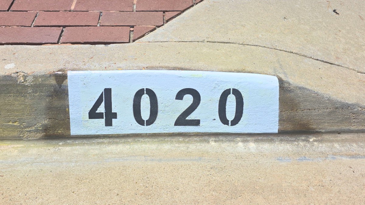 Black number 4020 painted on a white background curb address marker beside a brick paver walkway