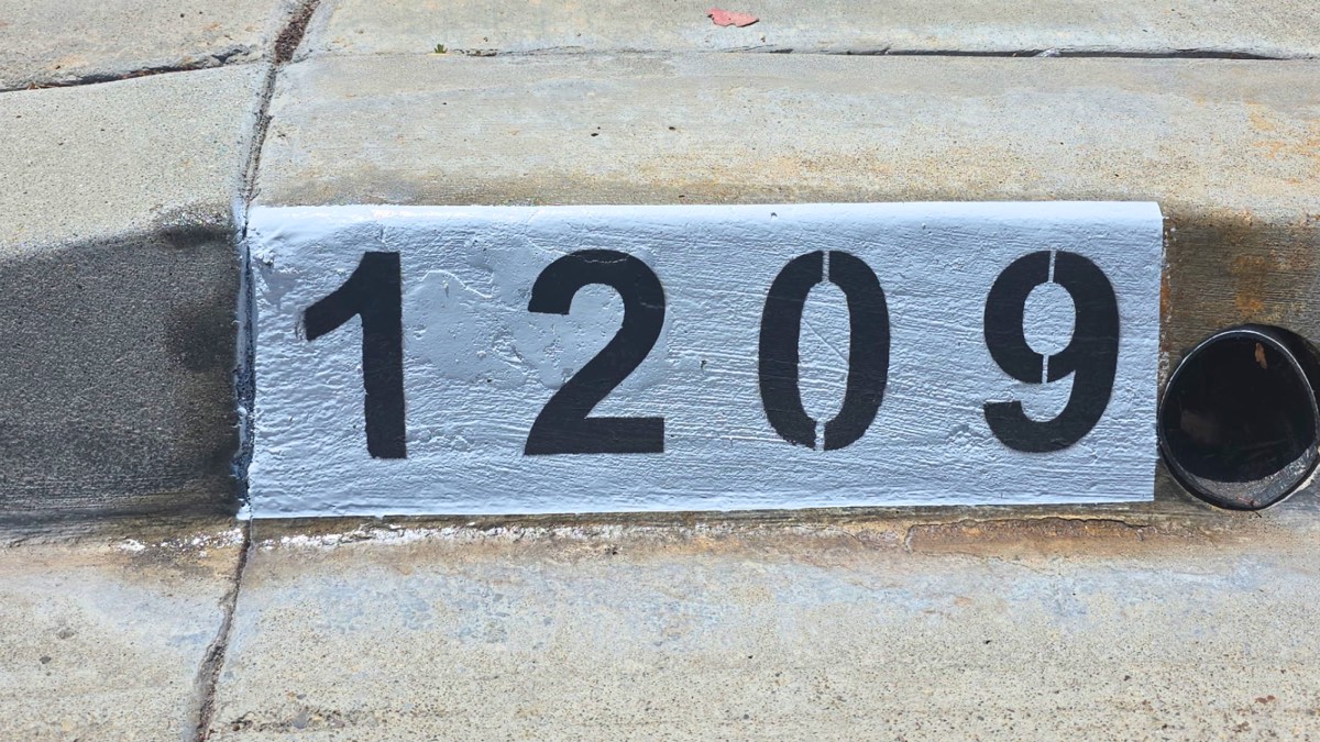 Black number 1209 painted on a white curb marker next to a cast iron drain cleanout pipe