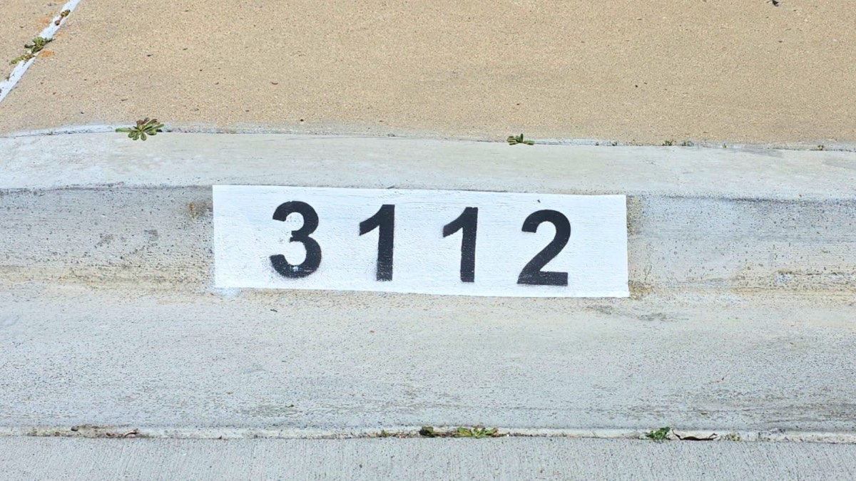 Black number 3112 painted on a white background curb marker along a sunlit residential street
