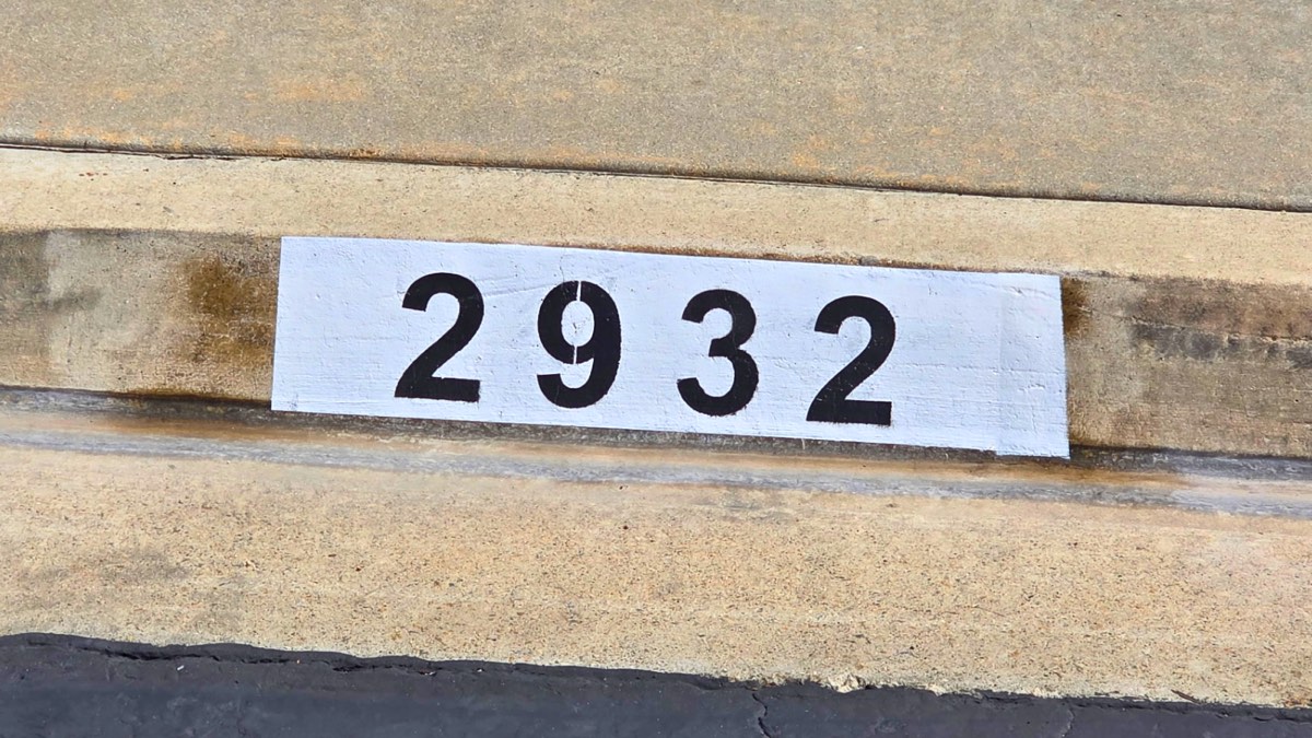 Black number 2932 painted on a white curb marker on an older, weathered concrete curb