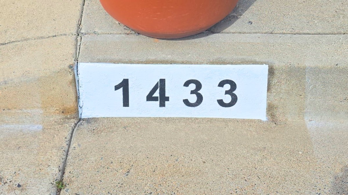 Black number 1433 painted on a white curb marker near a home's front entry pathway